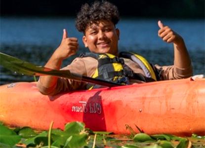 Hartwick College student in kayak smiling with thumbs up